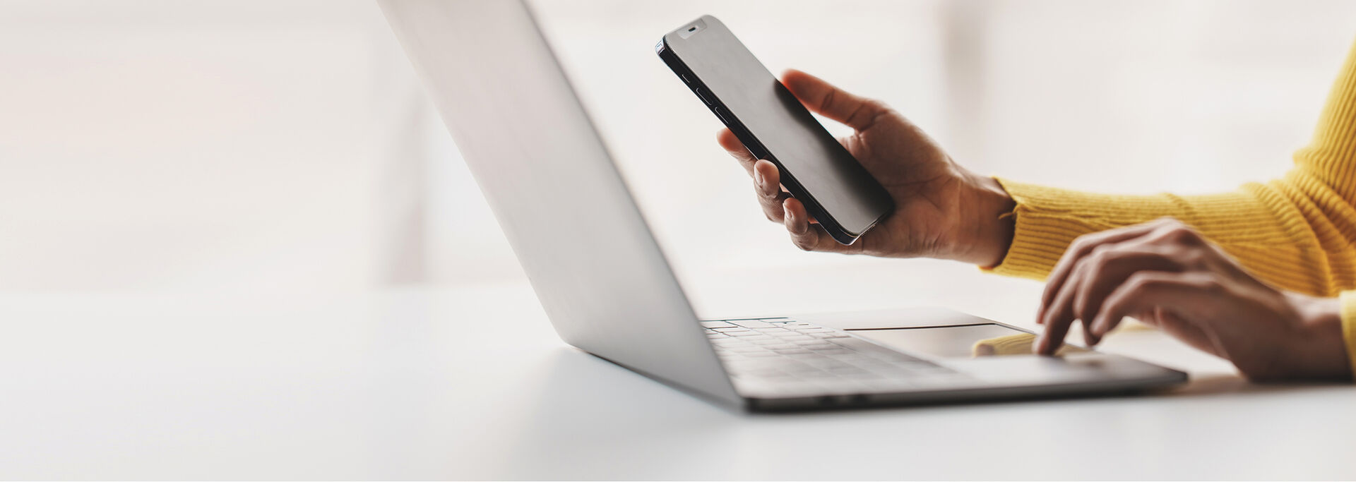Eine Hand hält ein Smartphone, während die andere Hand auf einer Laptop-Tastatur tippt.