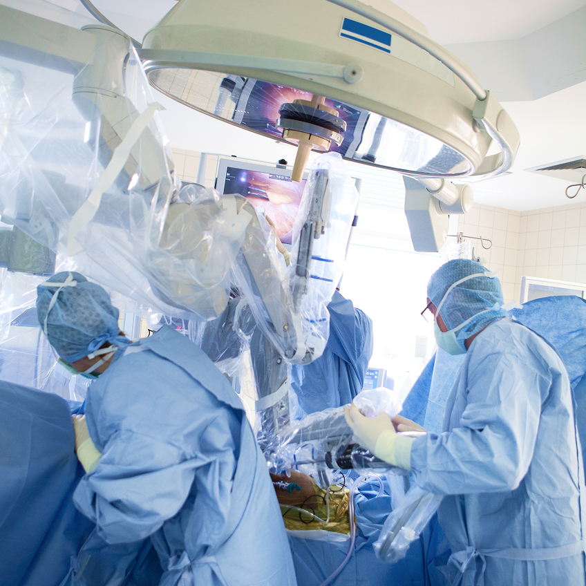 Chirurgisches Team in Schutzkleidung arbeitet an einem Patienten unter einem Operationsroboter.