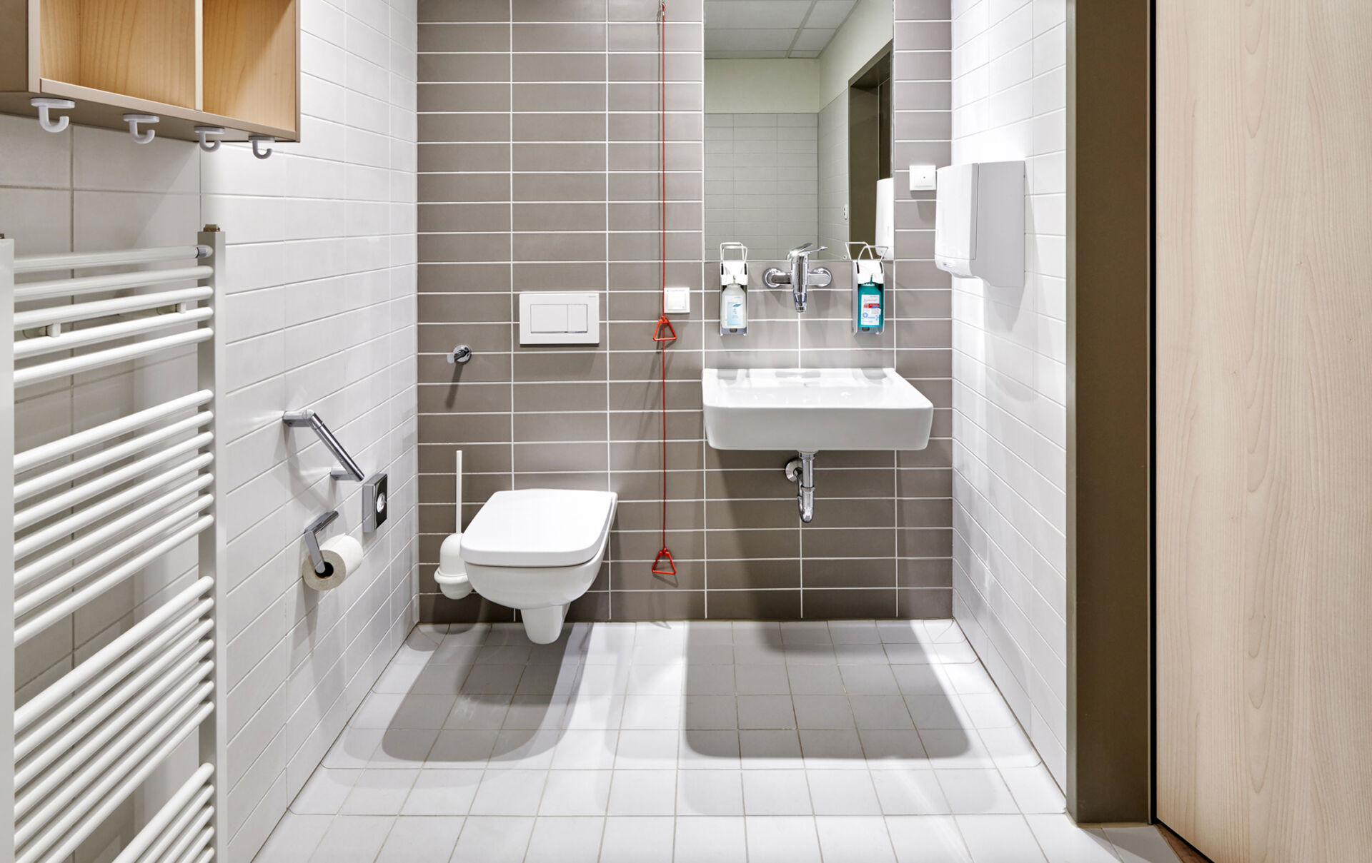 Modernes Badezimmer mit WC, Waschbecken, Handtuchhalter und grauen Fliesen.
