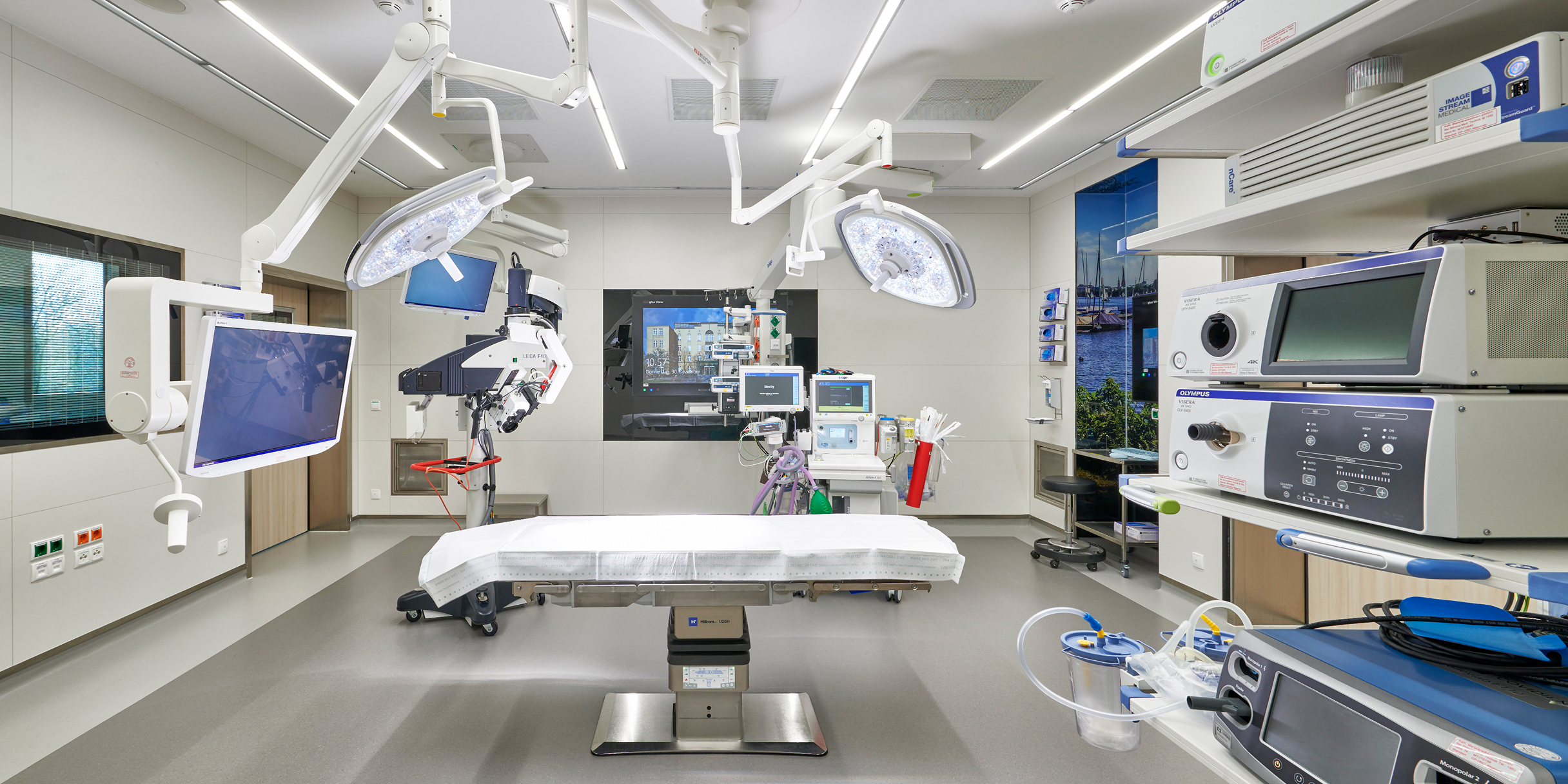 Moderne Operationssaal mit einem chirurgischen Tisch, medizinischen Geräten und Monitoren an Wänden und Decke.