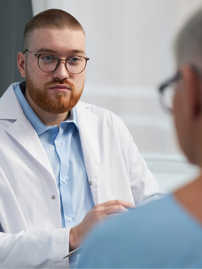 Ein Arzt im weißen Kittel spricht mit einem Patienten, der ihm gegenübersitzt.