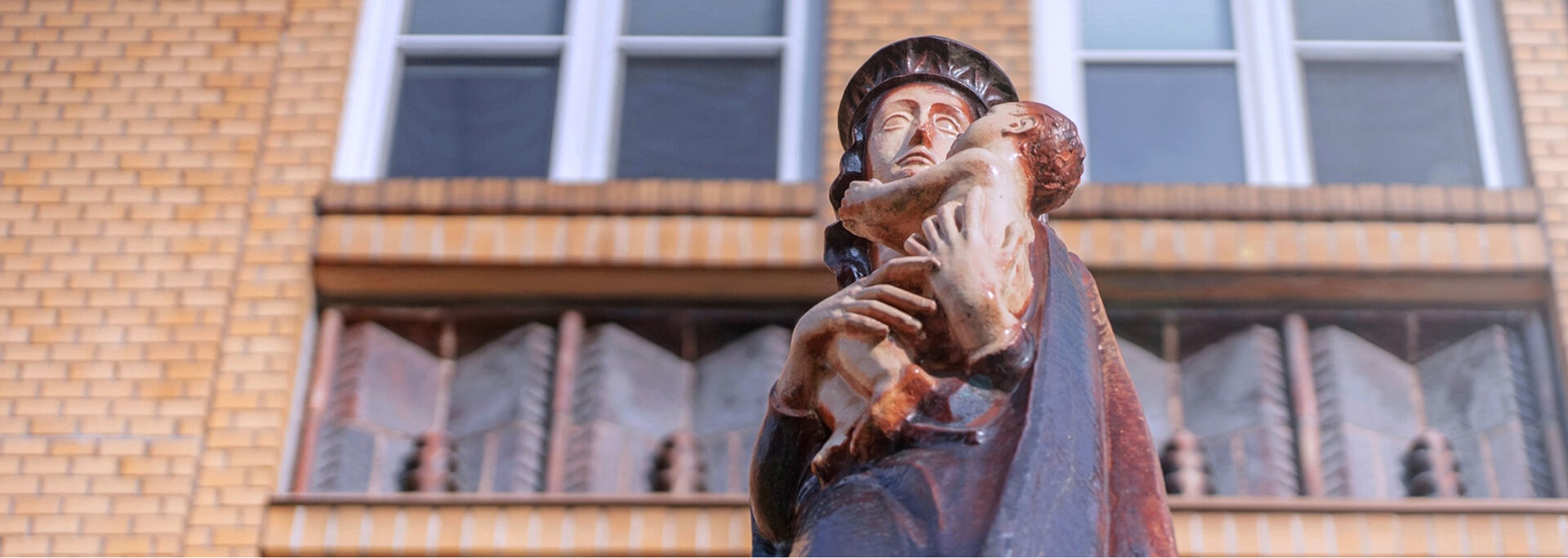 Statue einer Frau, die ein Kind in den Armen hält, sie steht vor einem Backsteingebäude mit Fenstern.