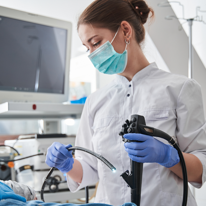 Eine medizinische Fachkraft in Schutzkleidung hält ein Endoskop und arbeitet an einem Patienten.