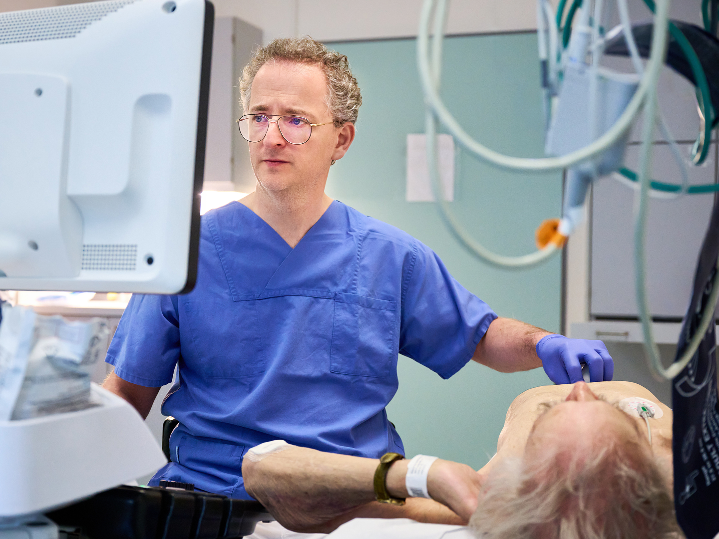 Ein Arzt in blauer Kleidung arbeitet an einem Computer, während er einen Patienten untersucht.