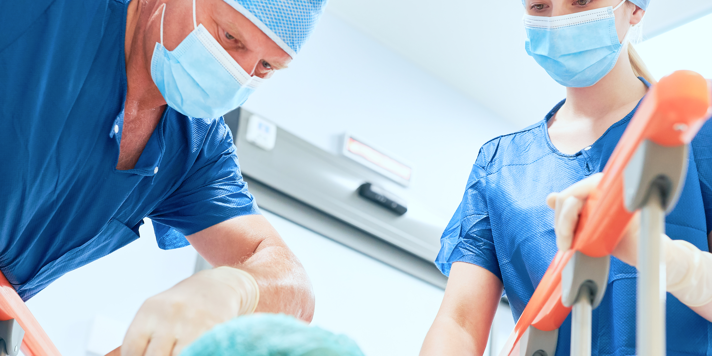 Zwei medizinische Fachkräfte in blauer Kleidung und Masken arbeiten konzentriert an einem Patienten.