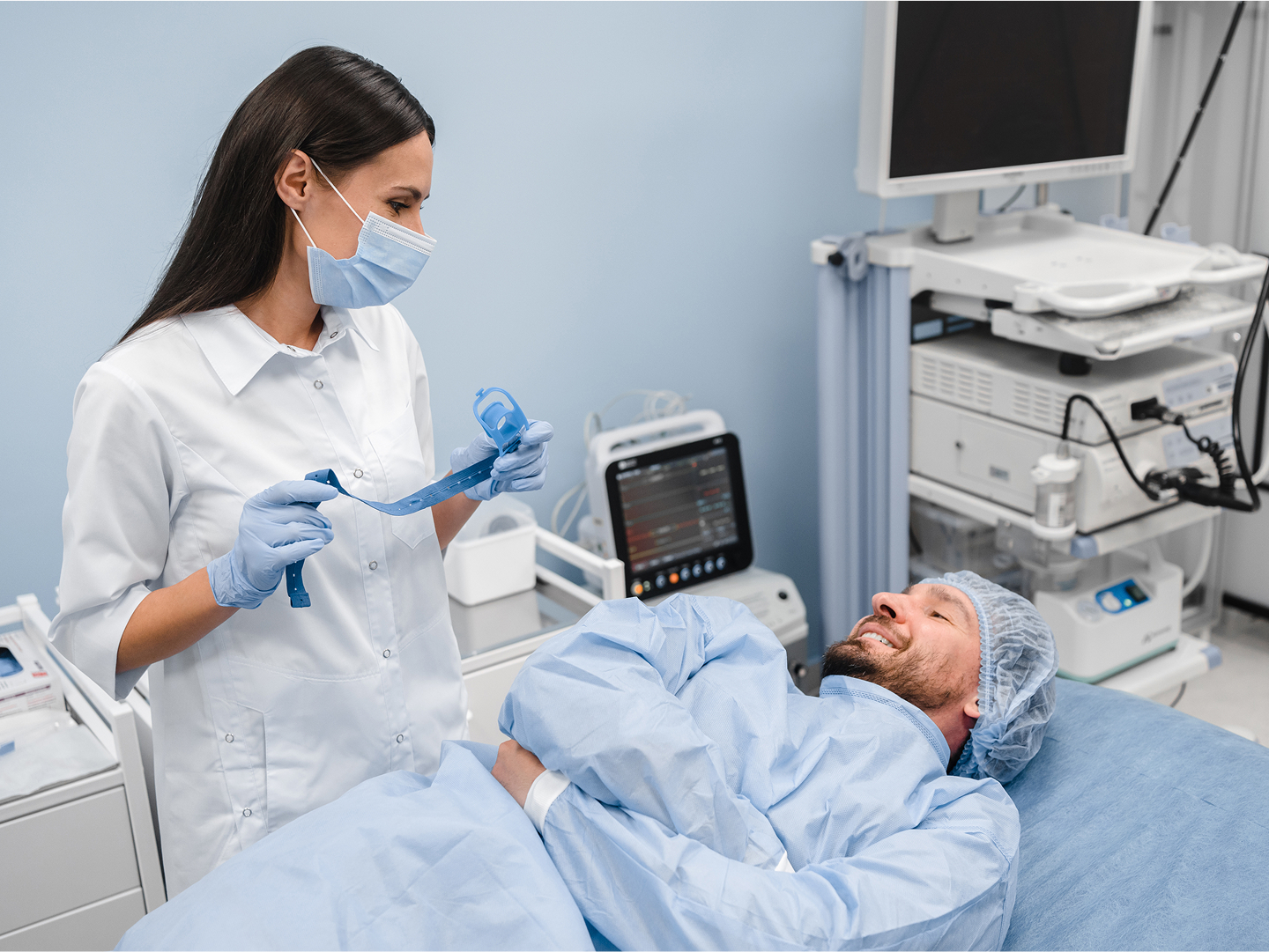 Eine medizinische Fachkraft spricht mit einem Patienten, der im Behandlungsraum auf einer Liege liegt.