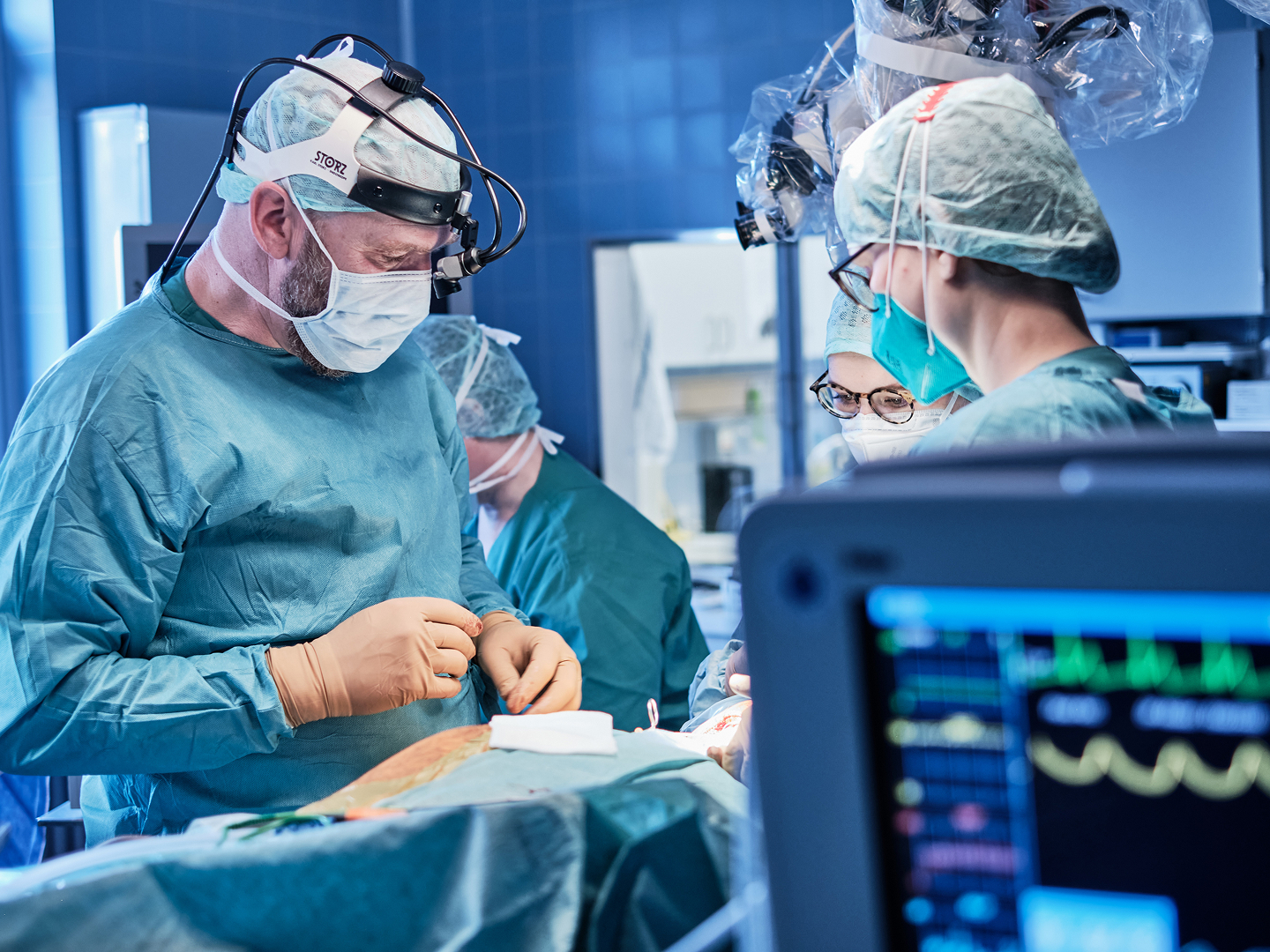 Chirurgisches Team in einem Operationssaal, das an einem Patienten arbeitet, mit medizinischen Geräten im Vordergrund.