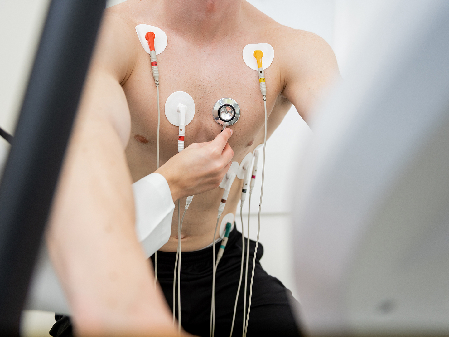 Ein Mann mit freiem Oberkörper erhält für eine medizinische Untersuchung Elektroden auf die Brust gesetzt.