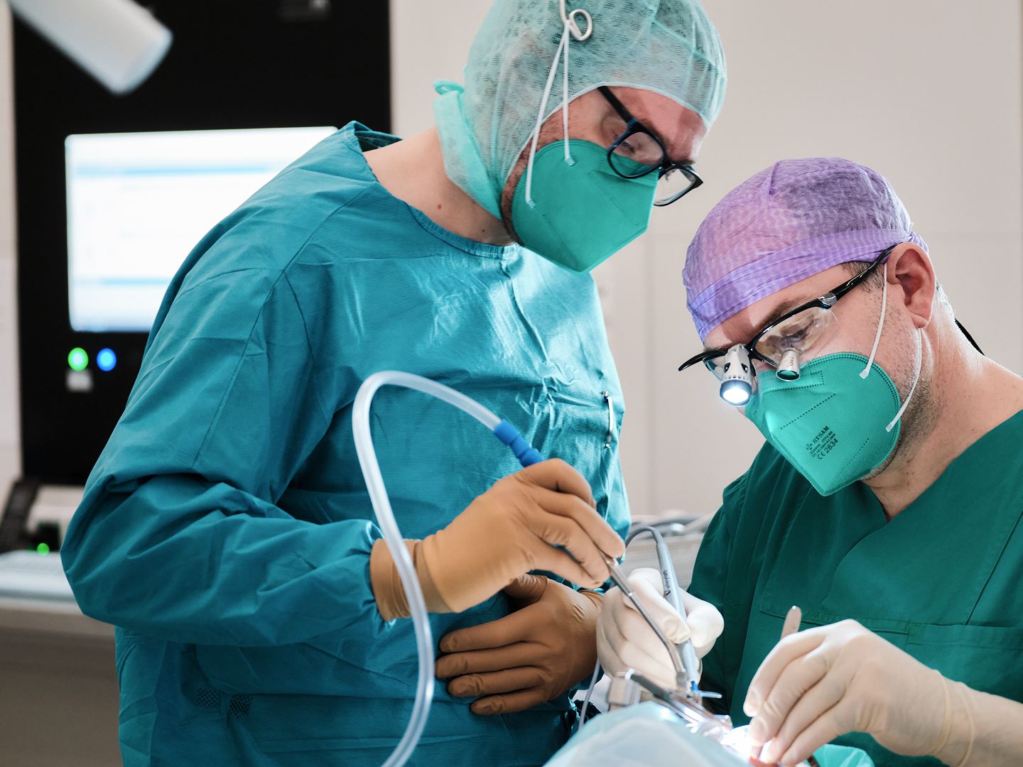 Zwei Chirurgen in OP-Kleidung und Masken führen einen Eingriff an einem Patienten durch.