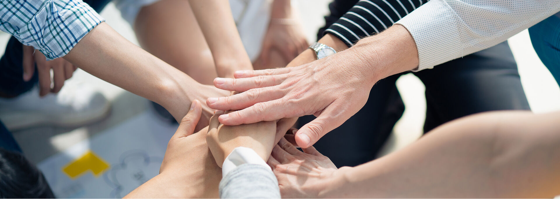 Mehrere Hände liegen übereinander, sie symbolisieren Zusammenarbeit und Gemeinschaft.