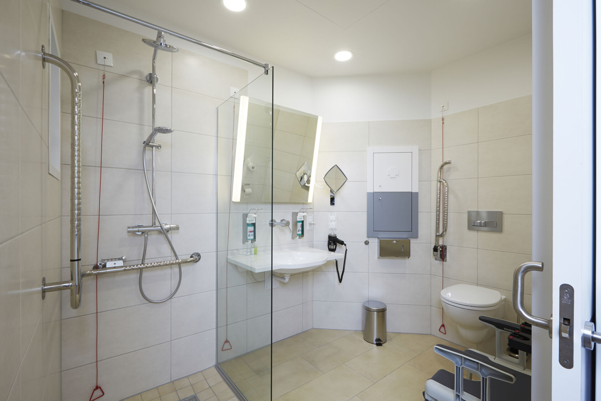 Barrierefreies Badezimmer mit Dusche, Haltegriffen, Waschbecken und WC. Helle, moderne Ausstattung.