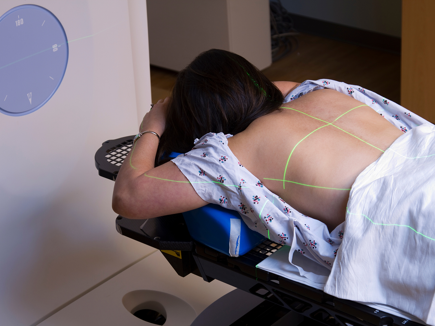 Eine Person liegt auf einem Behandlungstisch, bekleidet mit einem Krankenhaushemd, mit Laserlinien auf dem Rücken.