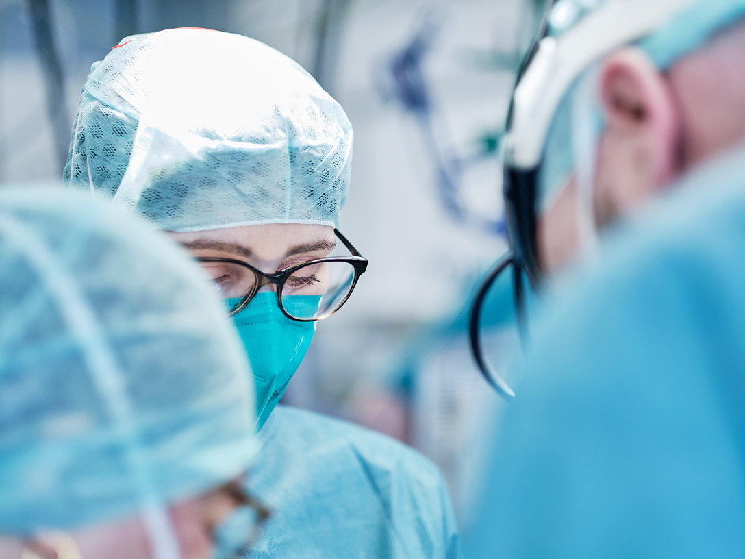 Chirurgisches Team in blauer Kleidung und Schutzmasken, konzentriert bei einer Operation.