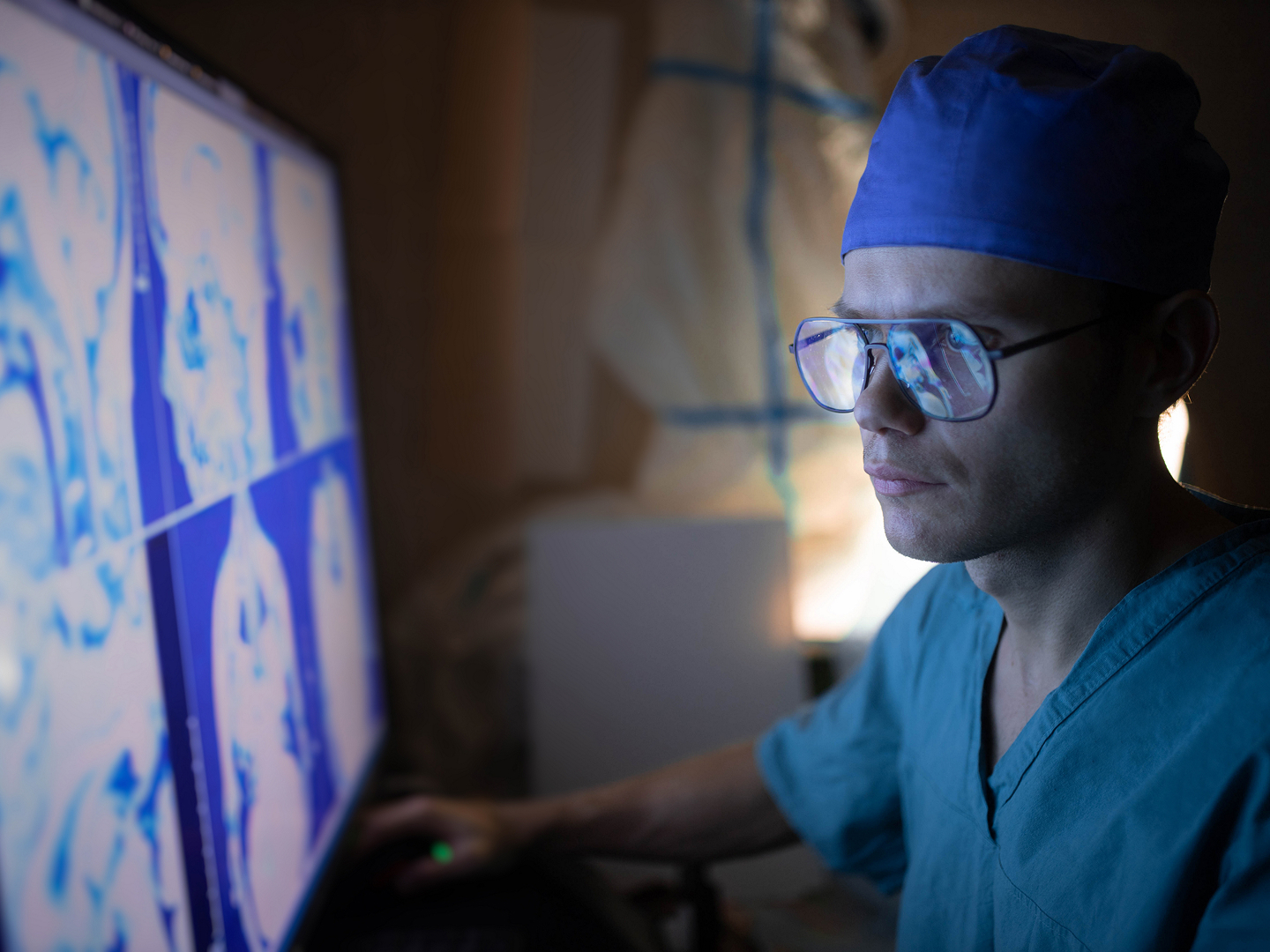 Ein junger Arzt mit Brille betrachtet konzentriert medizinische Bilder auf einem Computerbildschirm.