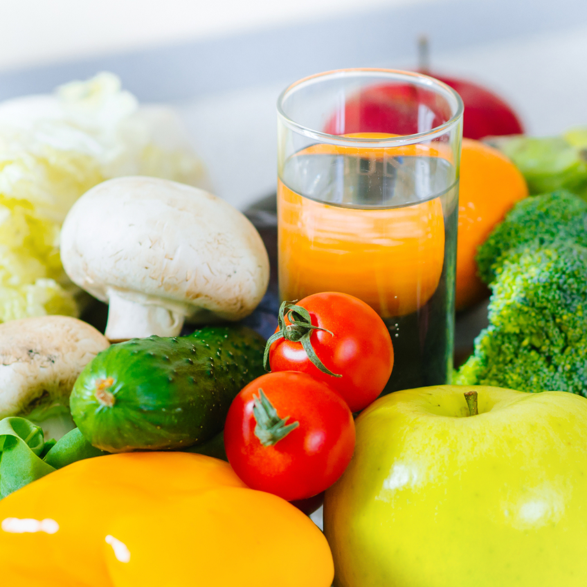 Bunte Auswahl an frischem Gemüse und Obst, darunter Brokkoli, Tomaten, Gurken, Paprika und ein Glas Wasser.