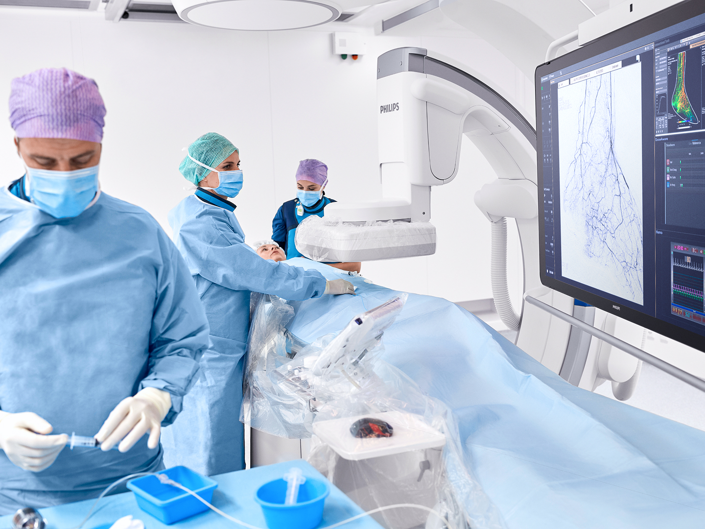 Medizinisches Team in OP-Kleidung arbeitet an einem Patienten, während ein Monitor medizinische Bilder anzeigt.