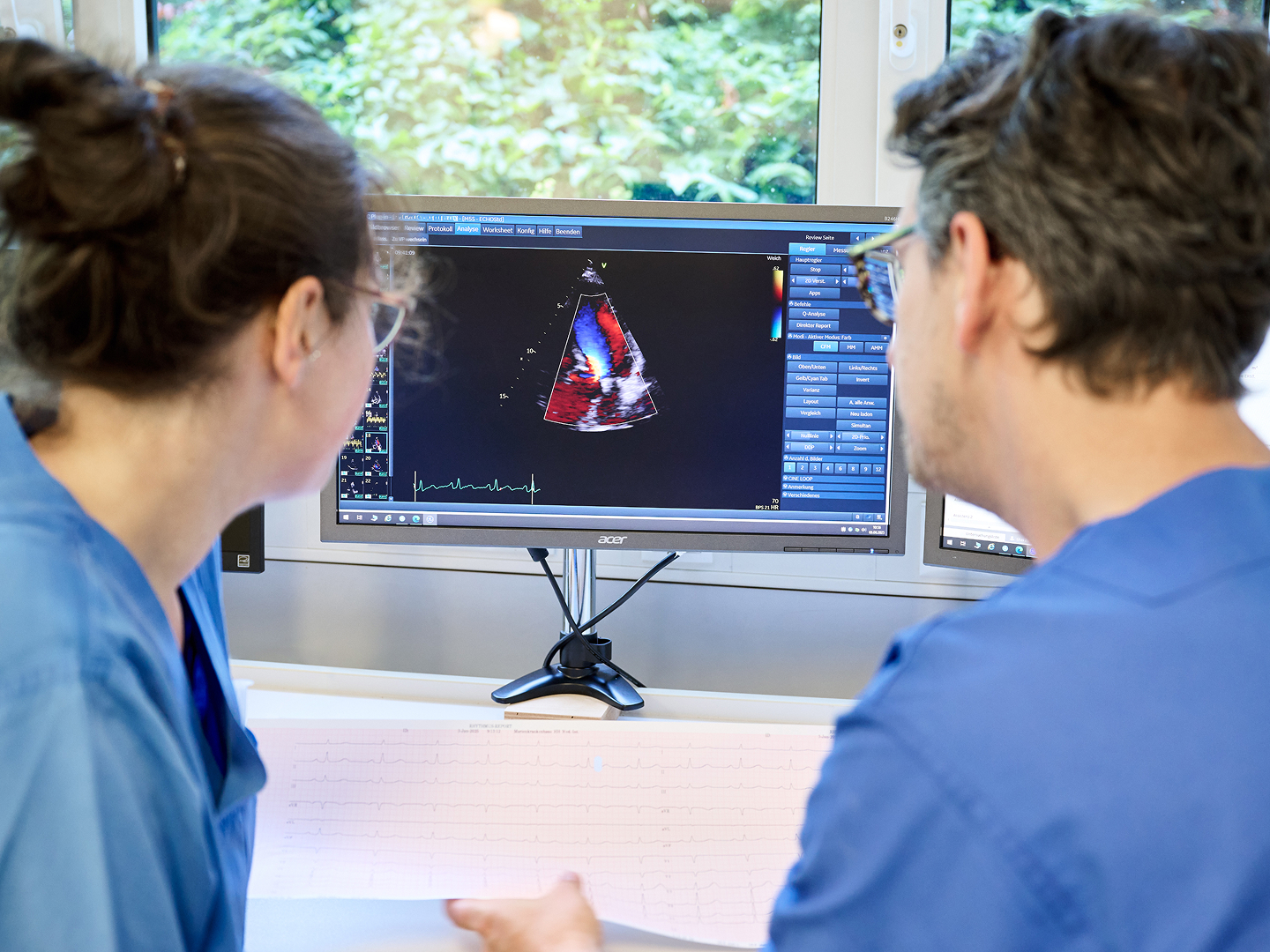 Zwei Personen in blauer Arbeitskleidung betrachten gemeinsam ein medizinisches Bild auf einem Computerbildschirm.