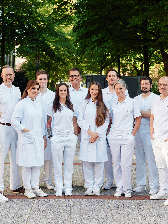 Gruppe von Personen in weißer Arbeitskleidung steht im Freien, umgeben von Bäumen.