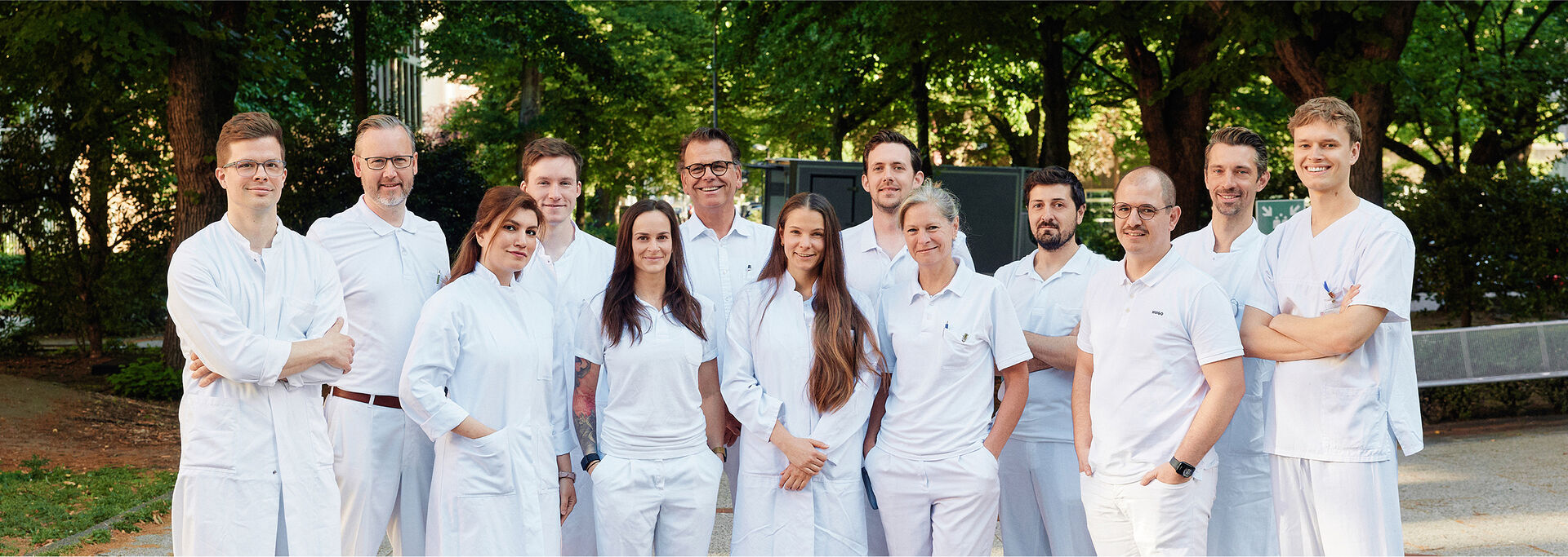 Gruppe von Personen in weißer Arbeitskleidung steht im Freien, umgeben von Bäumen und Grün.