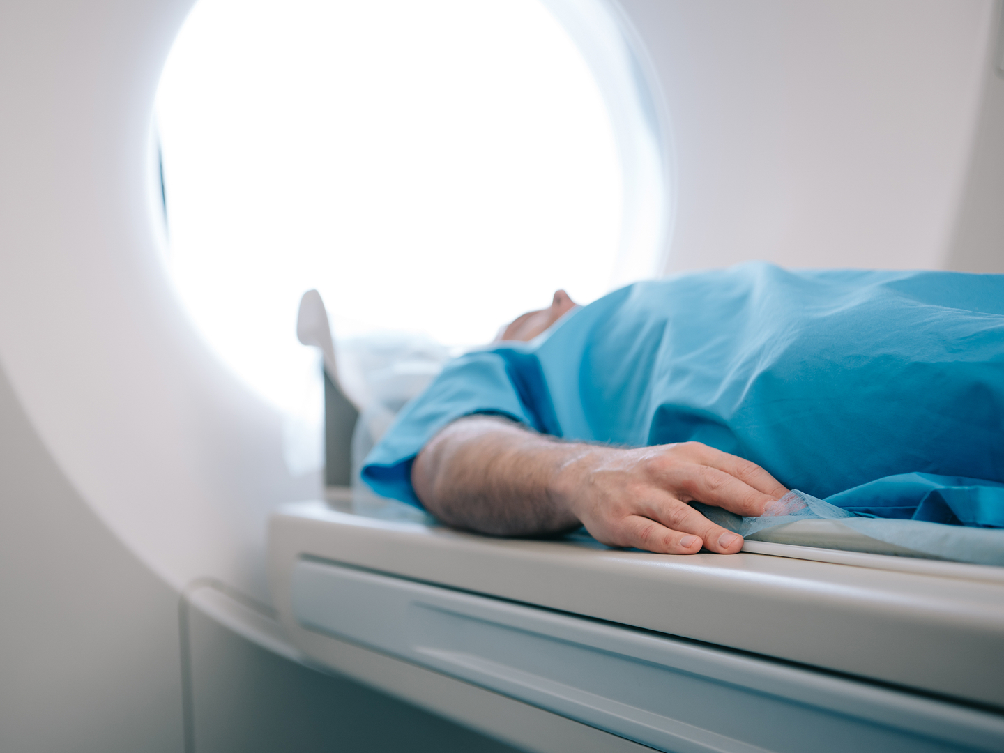 Patient in einem blauen Krankenhaushemd liegt auf der Liege eines CT-Gerätes.