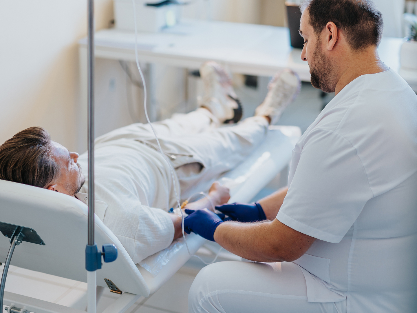 Ein Patient liegt auf einer Liege, während ein Arzt ihm einen Zugang legt.