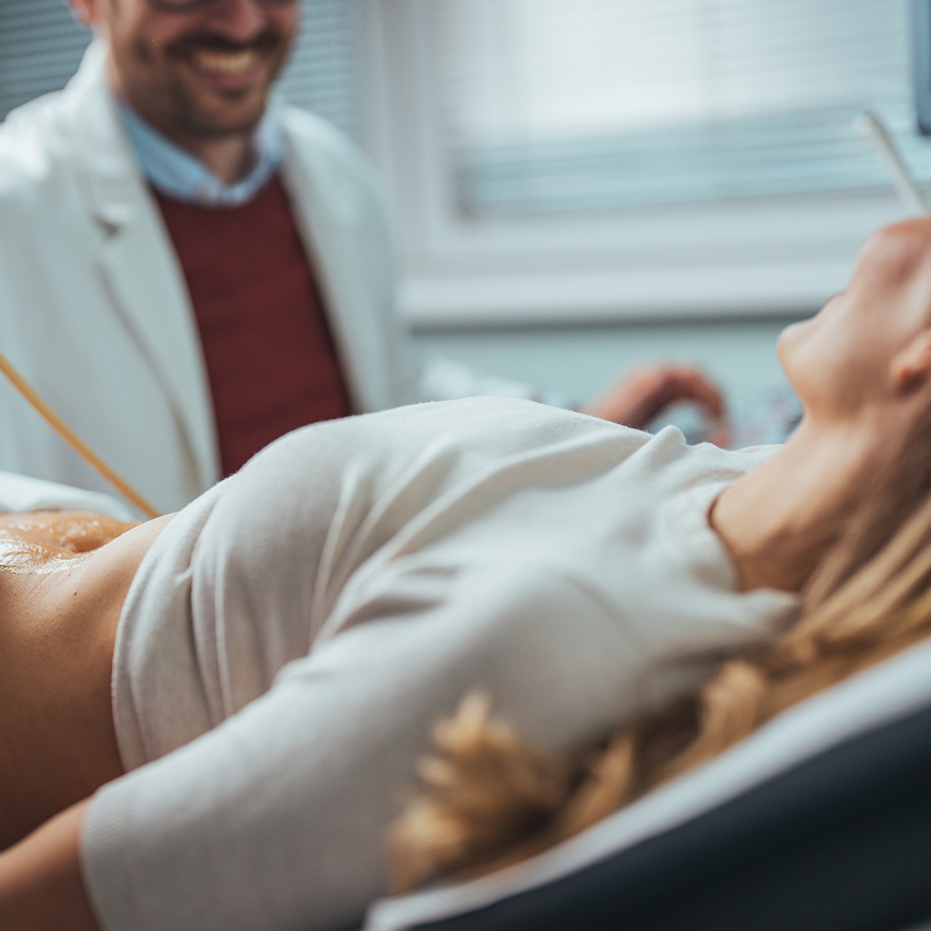 Ein Arzt lächelt, während eine Patientin auf einer Liege liegt und sich entspannt.