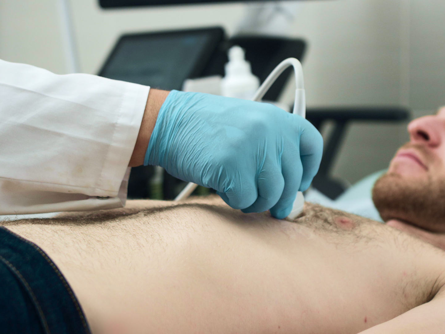 Ein Arzt führt einen Ultraschall an der Brust eines liegenden Patienten durch.