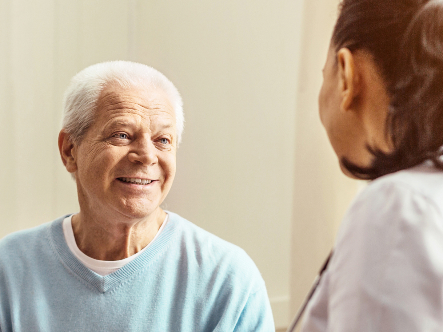 Ein älterer Patient lächelt während eines Gesprächs mit einer Ärztin im weißen Kittel, die ihm gegenübersitzt.