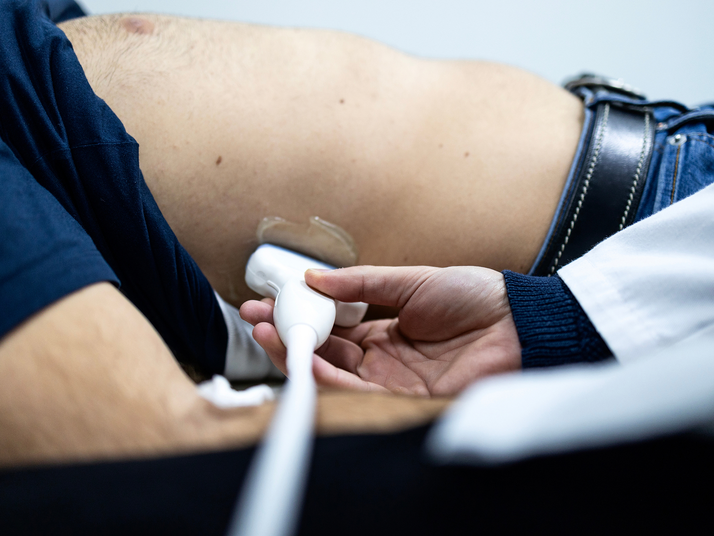Ein Arzt führt einen Ultraschall an der rechten Rumpfseite eines liegenden Patienten durch.