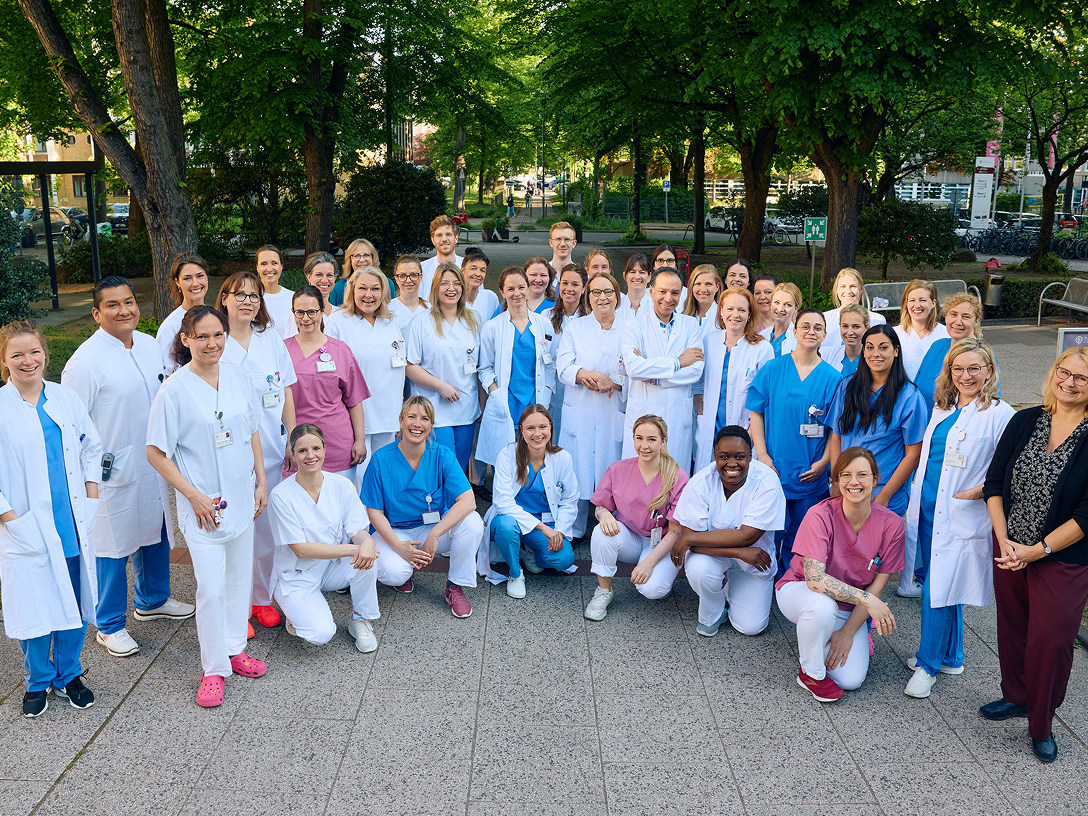 Eine Gruppe von medizinischem Personal in Arbeitskleidung steht vor der Klinik. Alle lächeln und schauen in die Kamera.