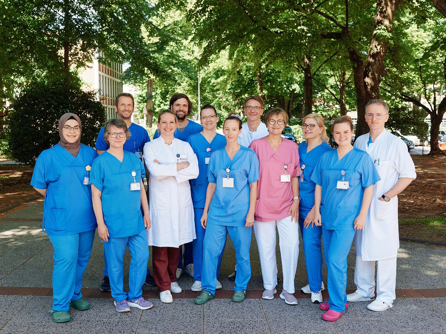 Gruppe von Personen in medizinischer Kleidung, posiert im Freien vor Bäumen.