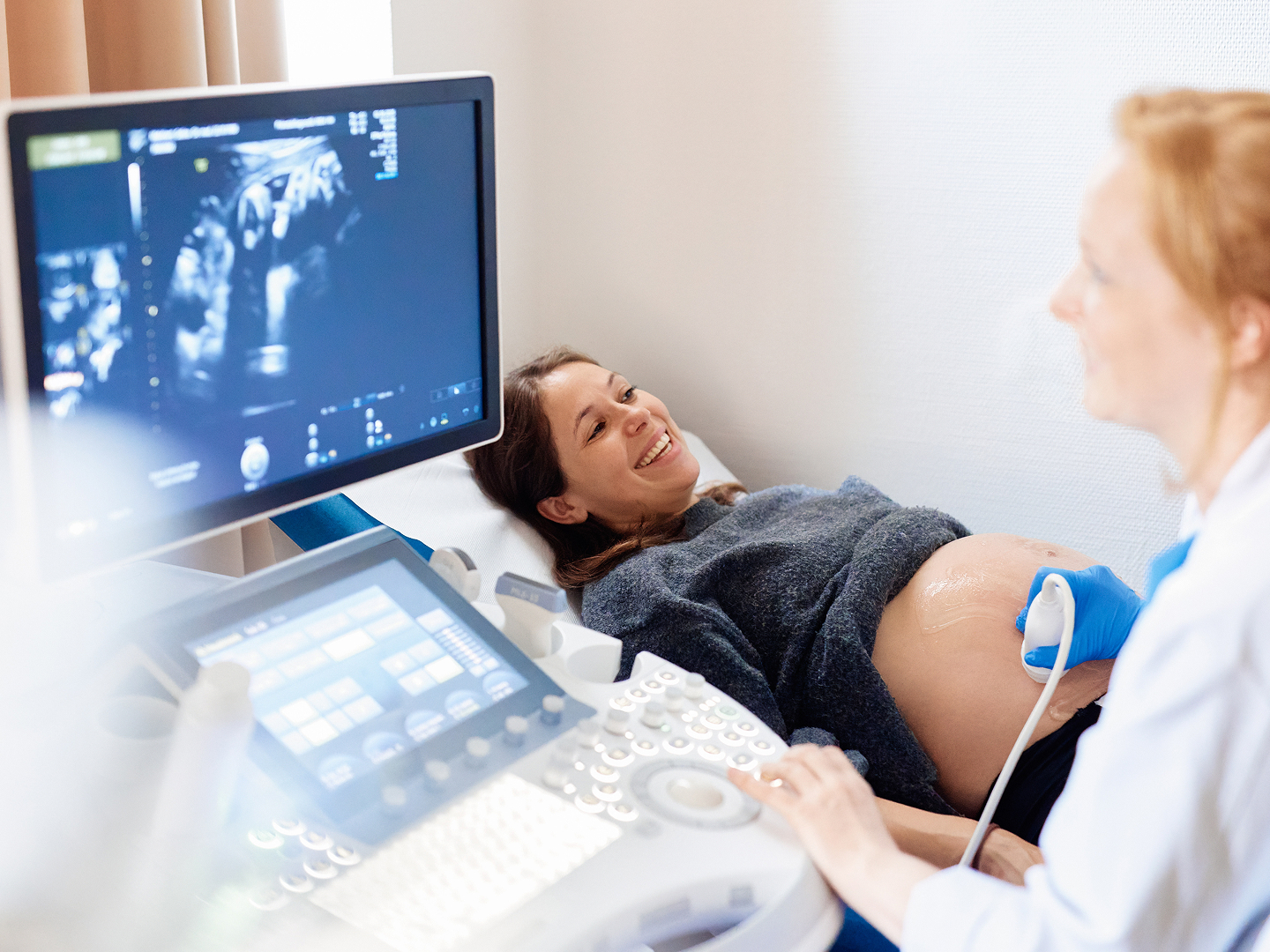 Schwangere Frau liegt auf einer Liege, während eine Ärztin mit einem Ultraschallgerät ihren Bauch untersucht.