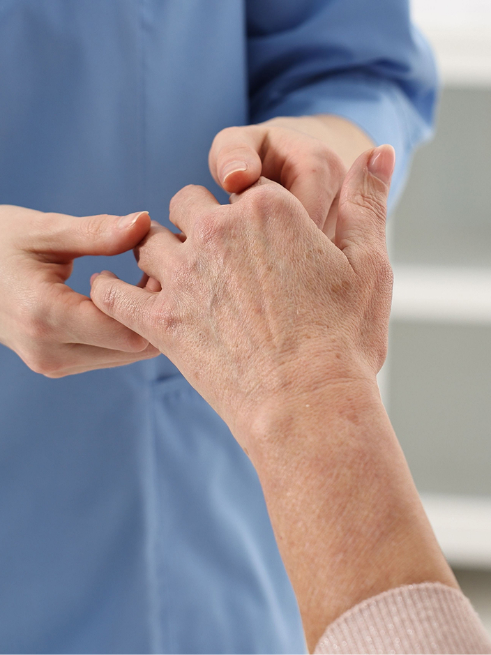 Eine Pflegekraft untersucht die Hand einer älteren Rheuma-Patientin.