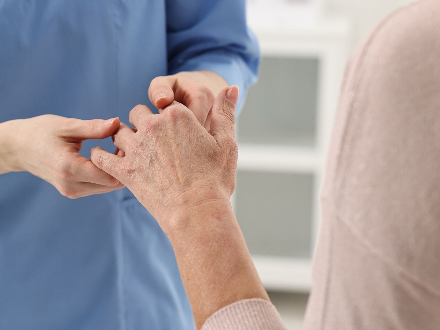 Eine Pflegekraft untersucht die Hand einer älteren Rheuma-Patientin.