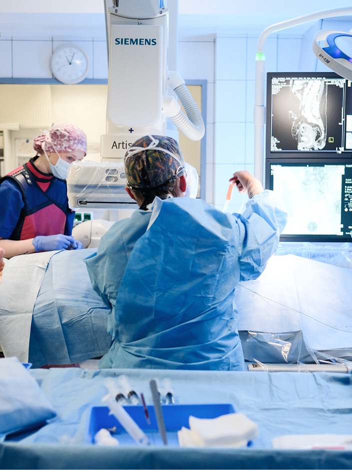 Chirurgisches Team in einem Operationssaal, das an einem Patienten arbeitet, umgeben von medizinischen Geräten.