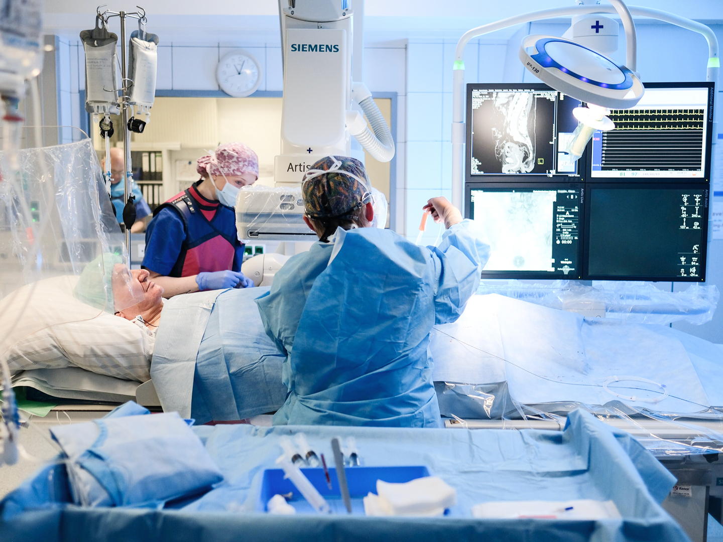 Chirurgisches Team in einem Operationssaal, das an einem Patienten arbeitet, umgeben von medizinischen Geräten.