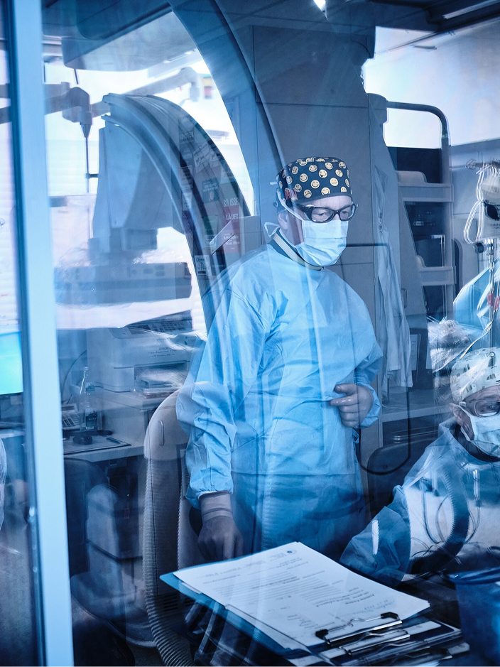 Ein medizinisches Fachpersonal in Schutzkleidung steht vor einem medizinischen Gerät in einem klinischen Umfeld.
