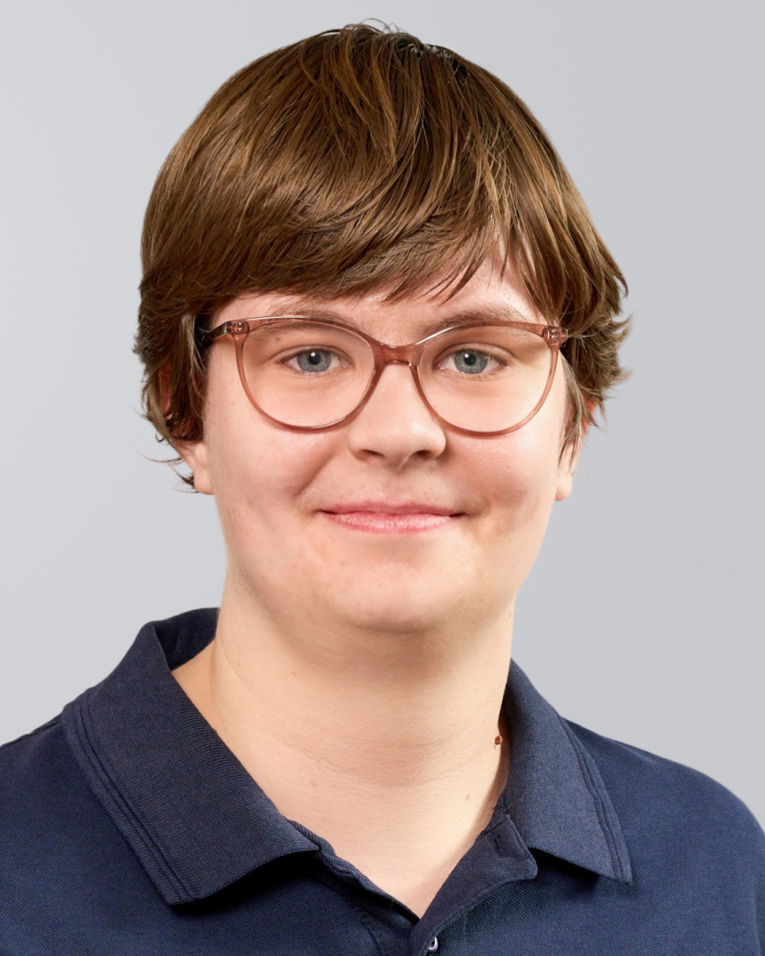 Person mit kurzen, braunen Haaren, Brille und dunkelblauen Polohemd vor einem neutralen Hintergrund.