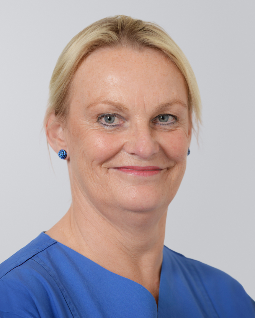 Frau mit blonden Haaren in blauer Kleidung lächelt vor einem hellen Hintergrund.