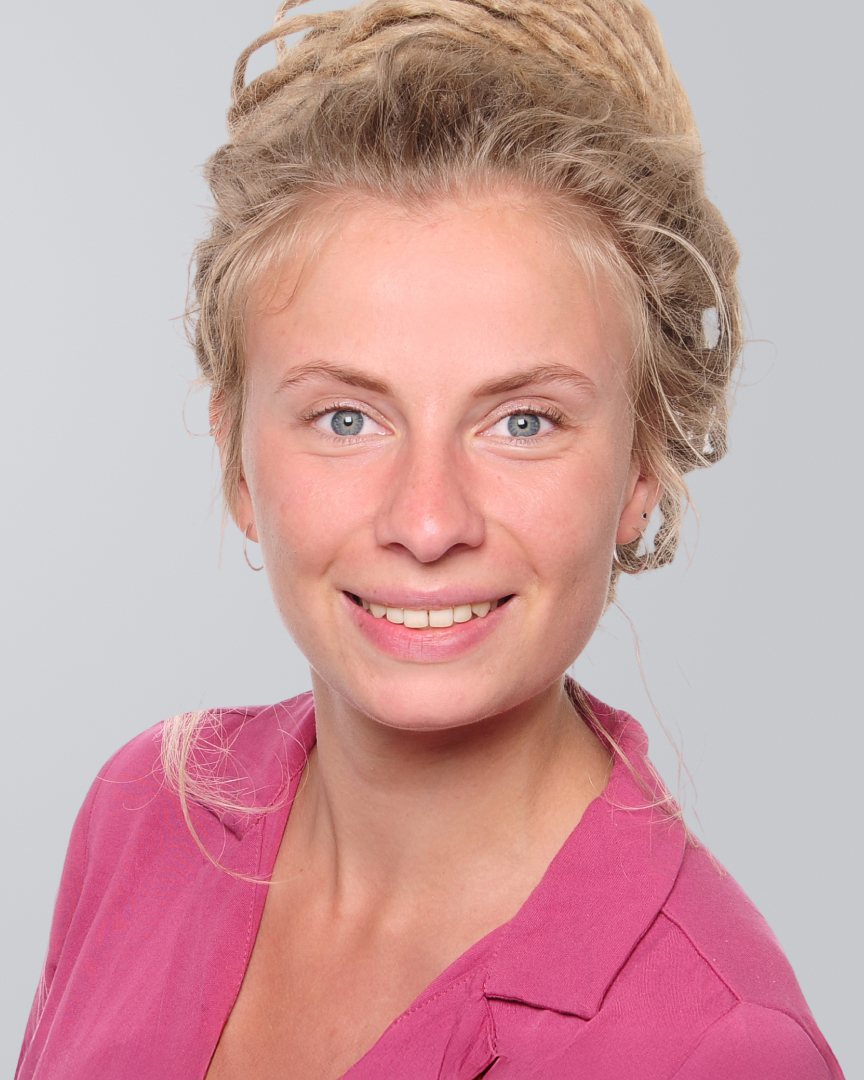 Lächelnde Frau mit blonden Haaren, die zu einem Dutt gebunden sind, und pinkem Oberteil vor einem grauen Hintergrund.