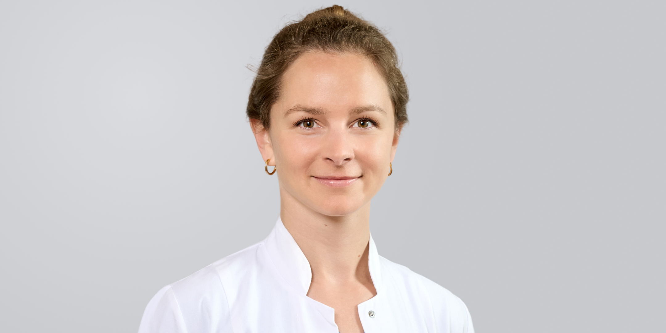 Porträt einer lächelnden Frau in einem weißen Kittel vor einem grauen Hintergrund.