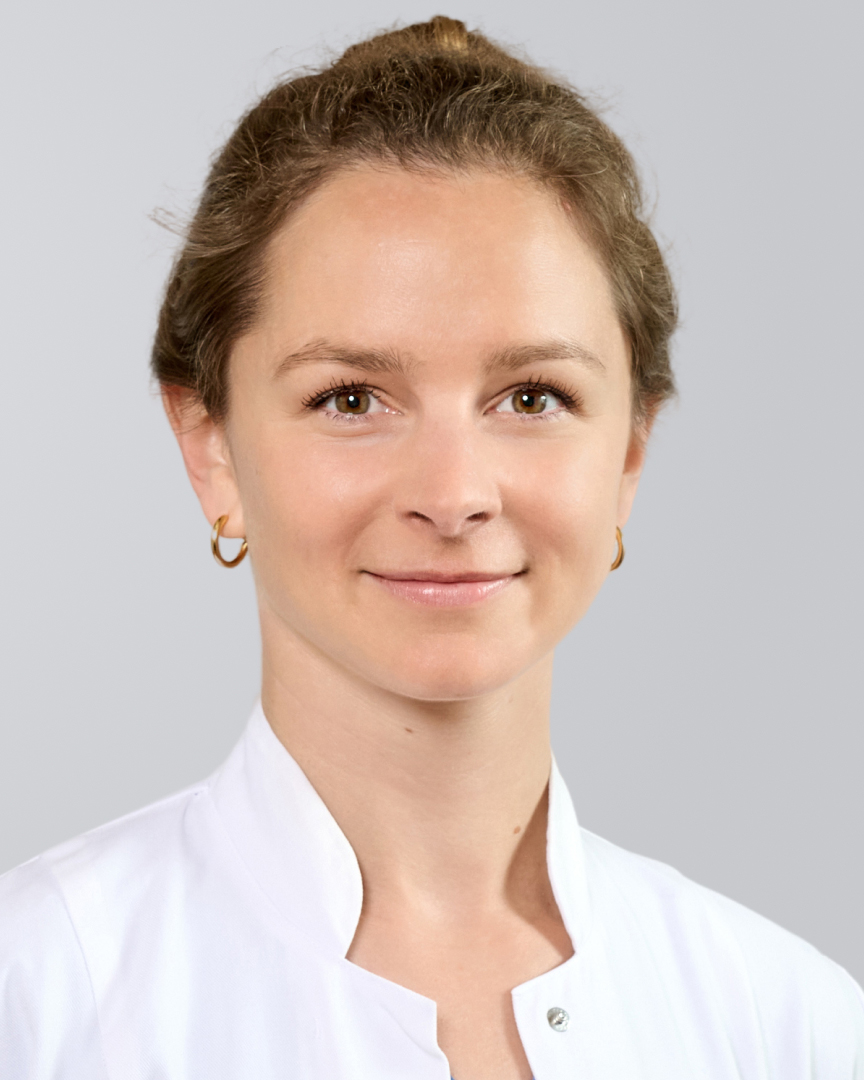 Porträt einer lächelnden Frau in einem weißen Kittel vor einem grauen Hintergrund.