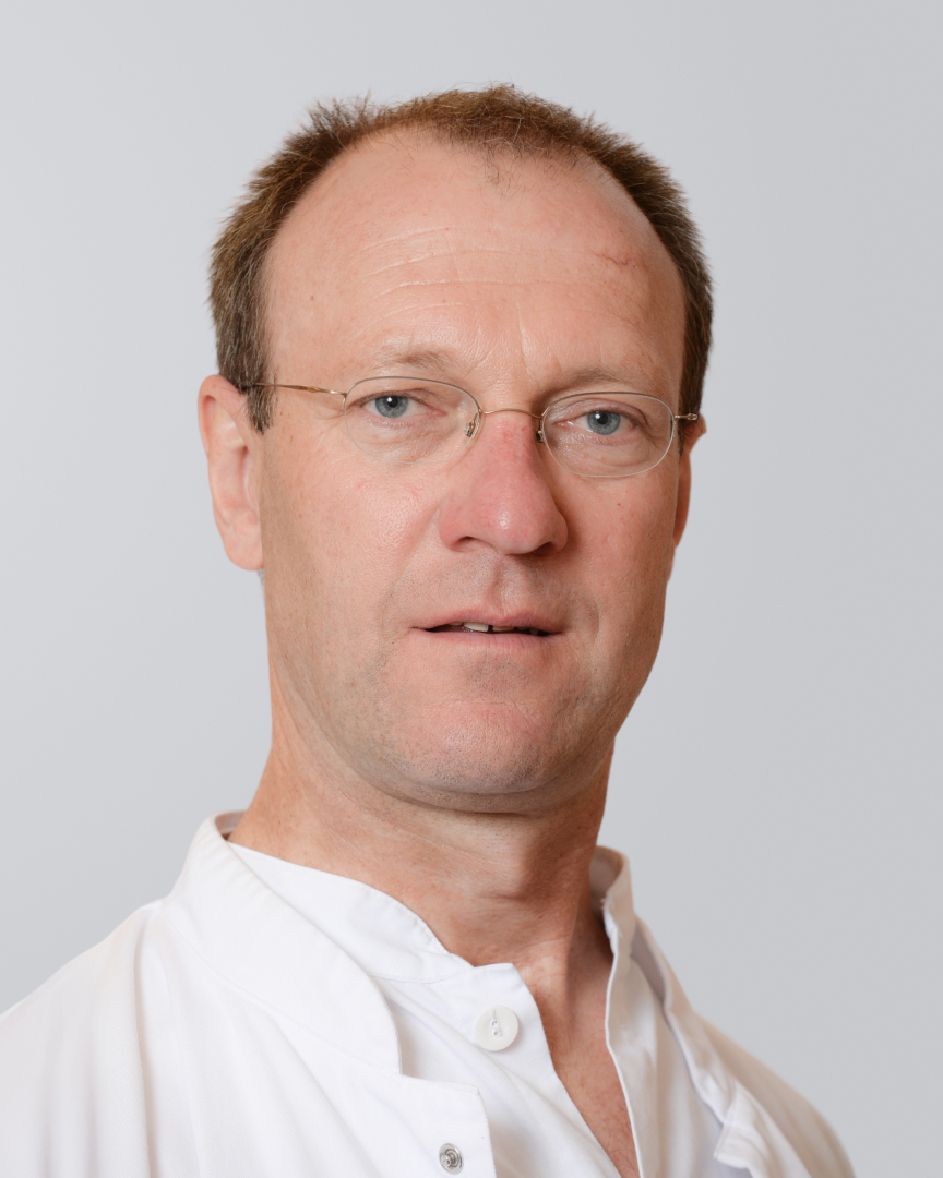 Porträt eines Mannes mit Brille und weißem Kittel vor einem neutralen Hintergrund.