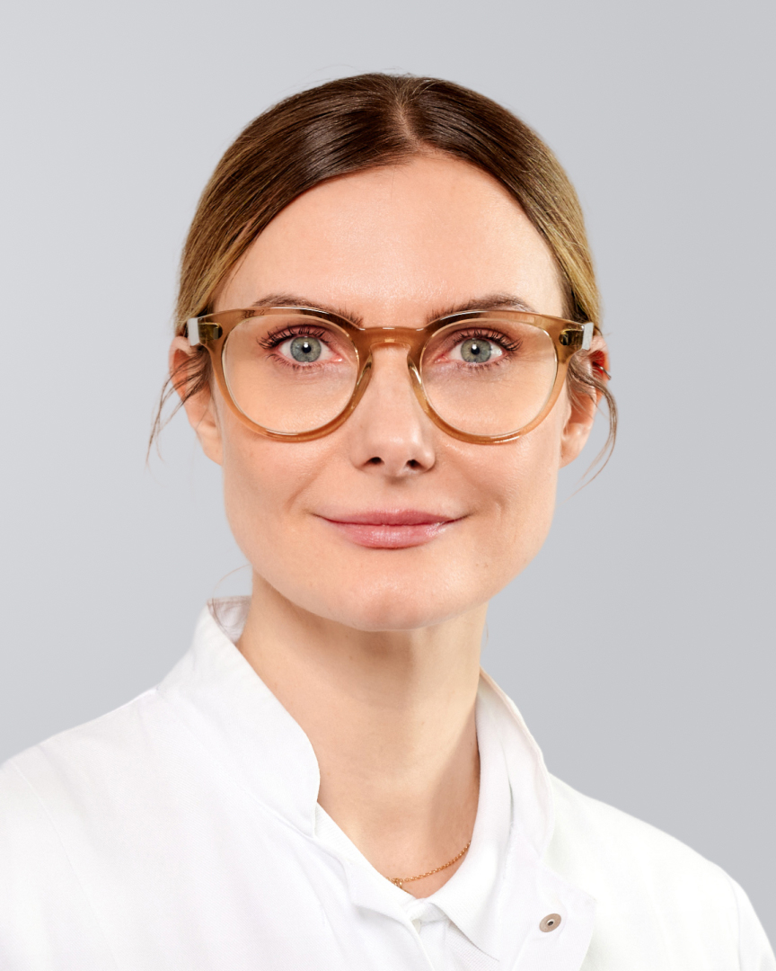 Lächelnde Frau mit Brille und dunkelblondem Haar vor einem grauen Hintergrund.