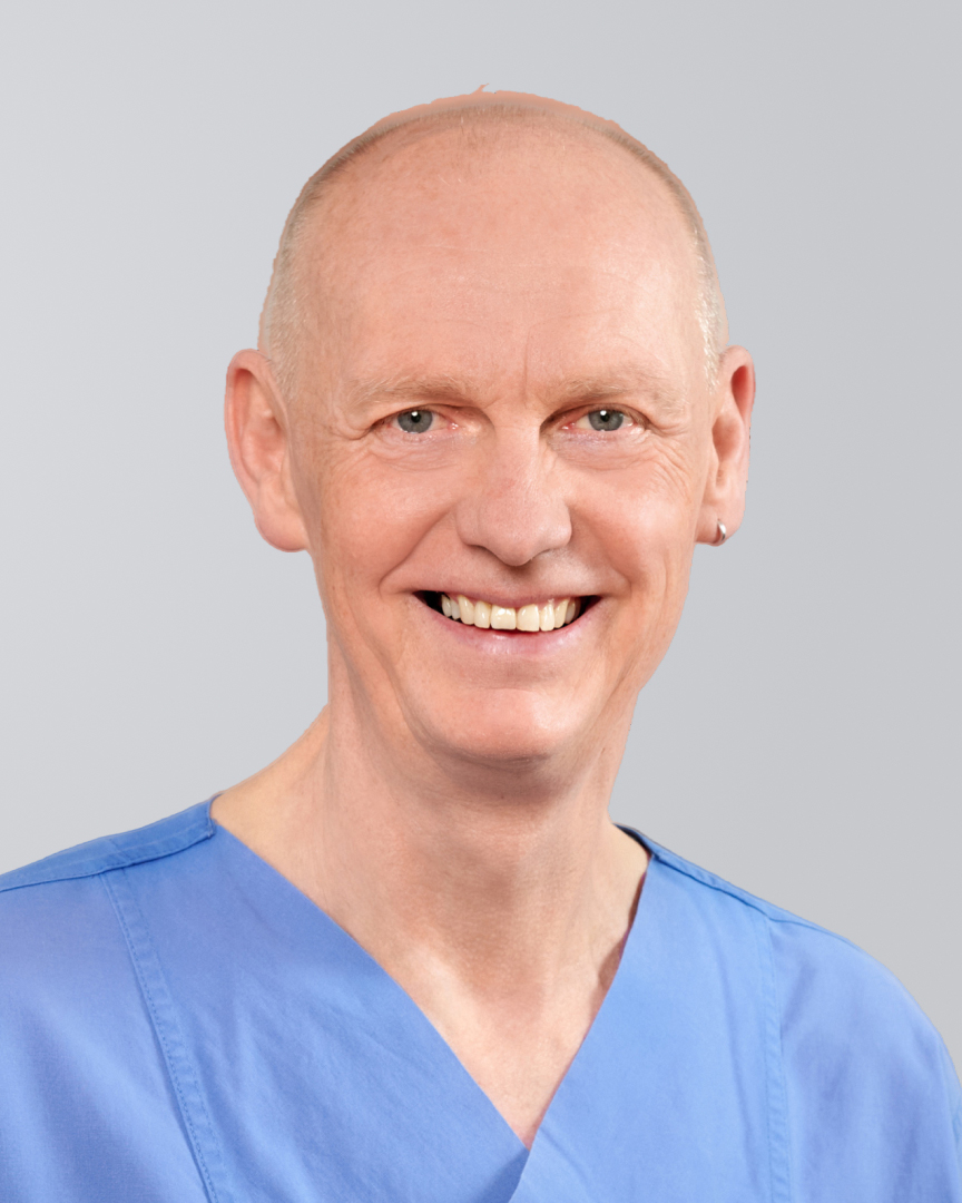 Lächelnder Mann mit Glatze und blauer Arbeitskleidung vor einem grauen Hintergrund.
