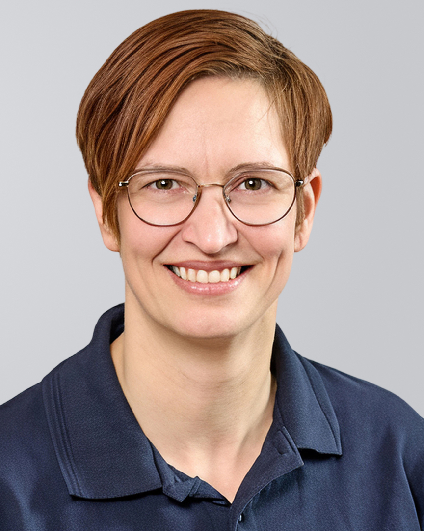 Frau mit kurzen, braunen Haaren, Brille und blauem Oberteil vor einem grauen Hintergrund.