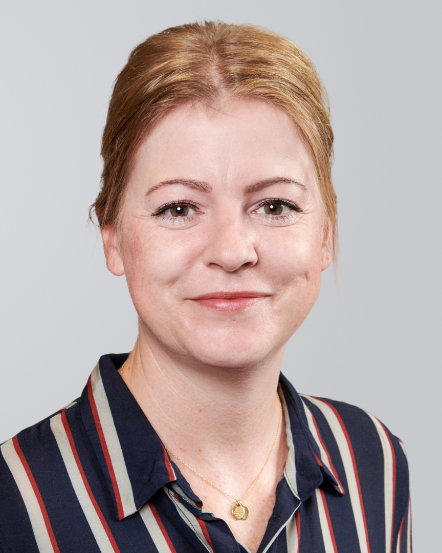 Porträt einer lächelnden Frau mit blonden Haaren, die eine gestreifte Bluse trägt.