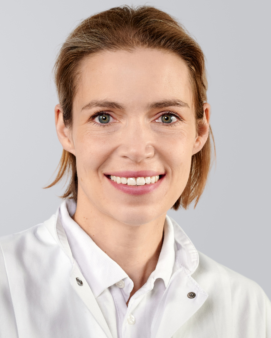 Lächelnde Frau in einem weißen Arztkittel vor einem grauen Hintergrund.