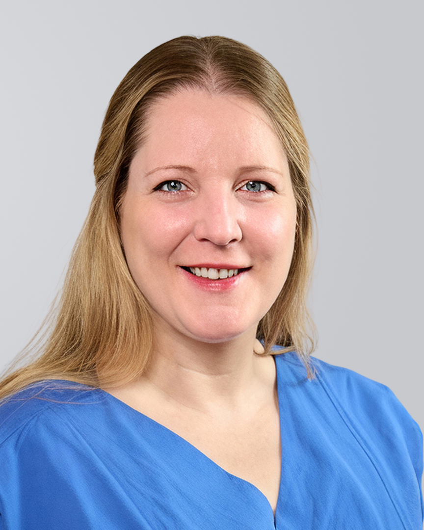Lächelnder Frau mit langen blonden Haaren und blauem Oberteil vor einem grauen Hintergrund.