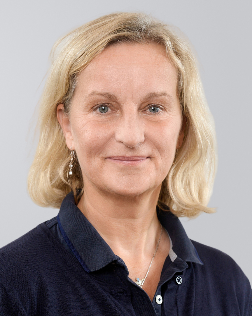 Porträt einer lächelnden Frau mit blonden Haarenund dunklem Polohemd vor einem neutralen Hintergrund.